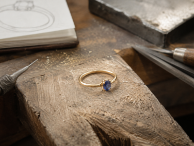Simple 9ct yellow gold engagement ring with small blue gemstone on a jeweller’s bench