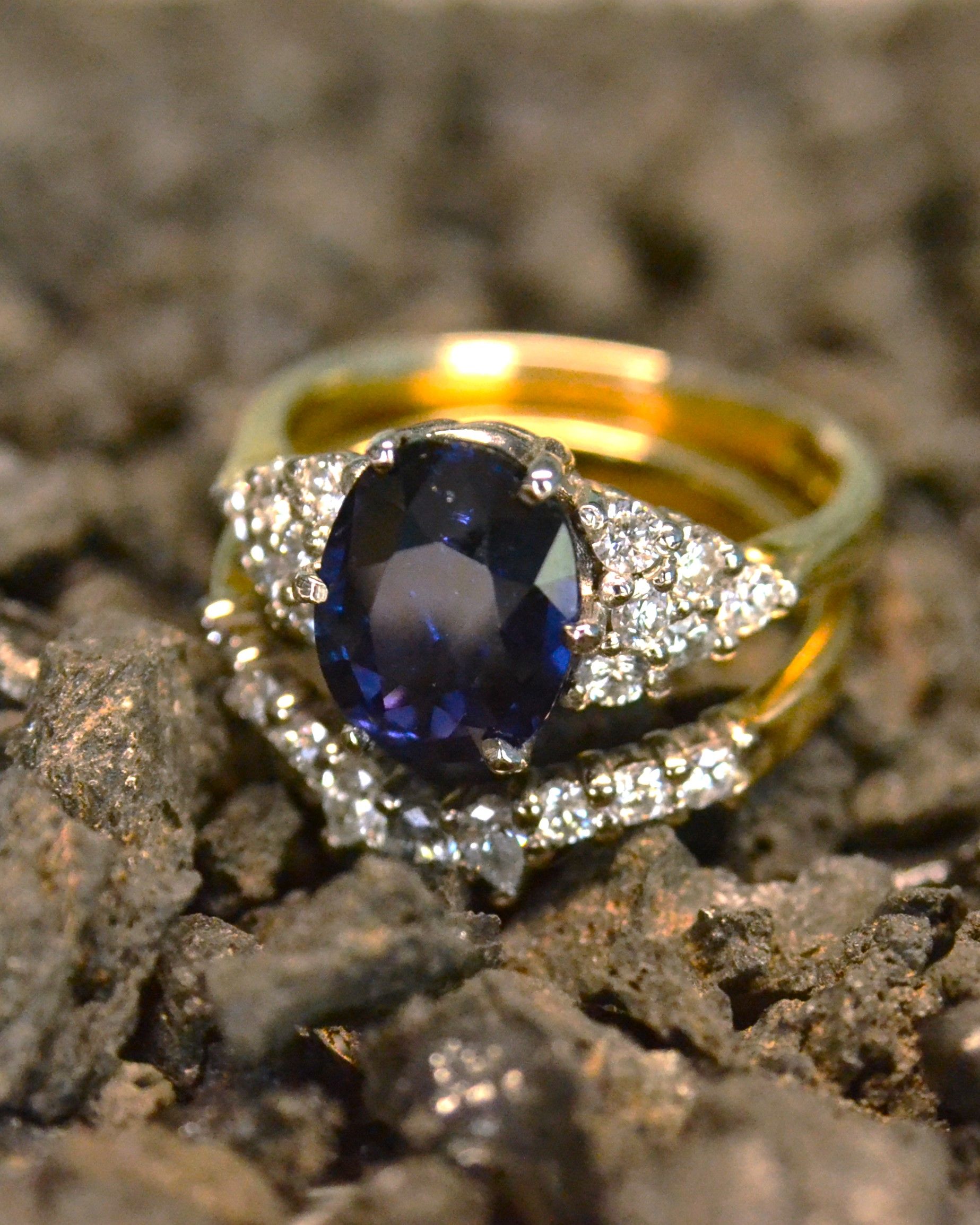 Handmade gold engagement ring with sapphire and fitted wedding band photographed in soil
