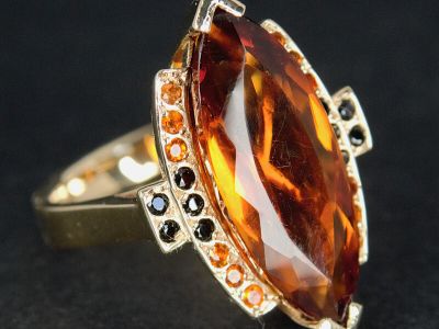 Vintage style yellow gold ring featuring a marquise cut citrine centre stone surrounded by black and orange accent gemstones on a dark background