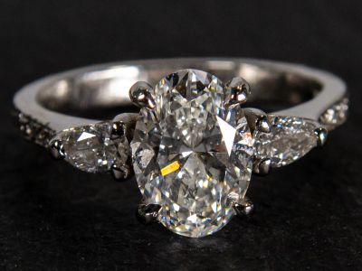 Handmade platinum engagement ring featuring an oval centre diamond with pear shaped diamond side stones and diamond set shoulders