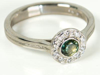 Three-quarter view of a platinum green sapphire engagement ring with diamond halo and tapered shoulders