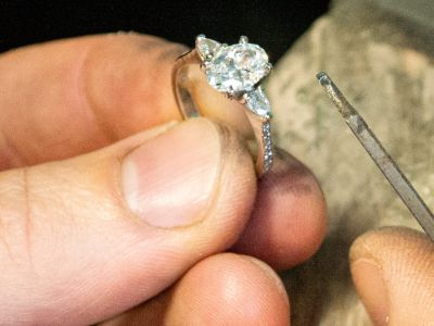 Close up of a goldsmith hand finishing a diamond engagement ring at the bench in a Wiltshire workshop, filing the setting in recycled precious metal