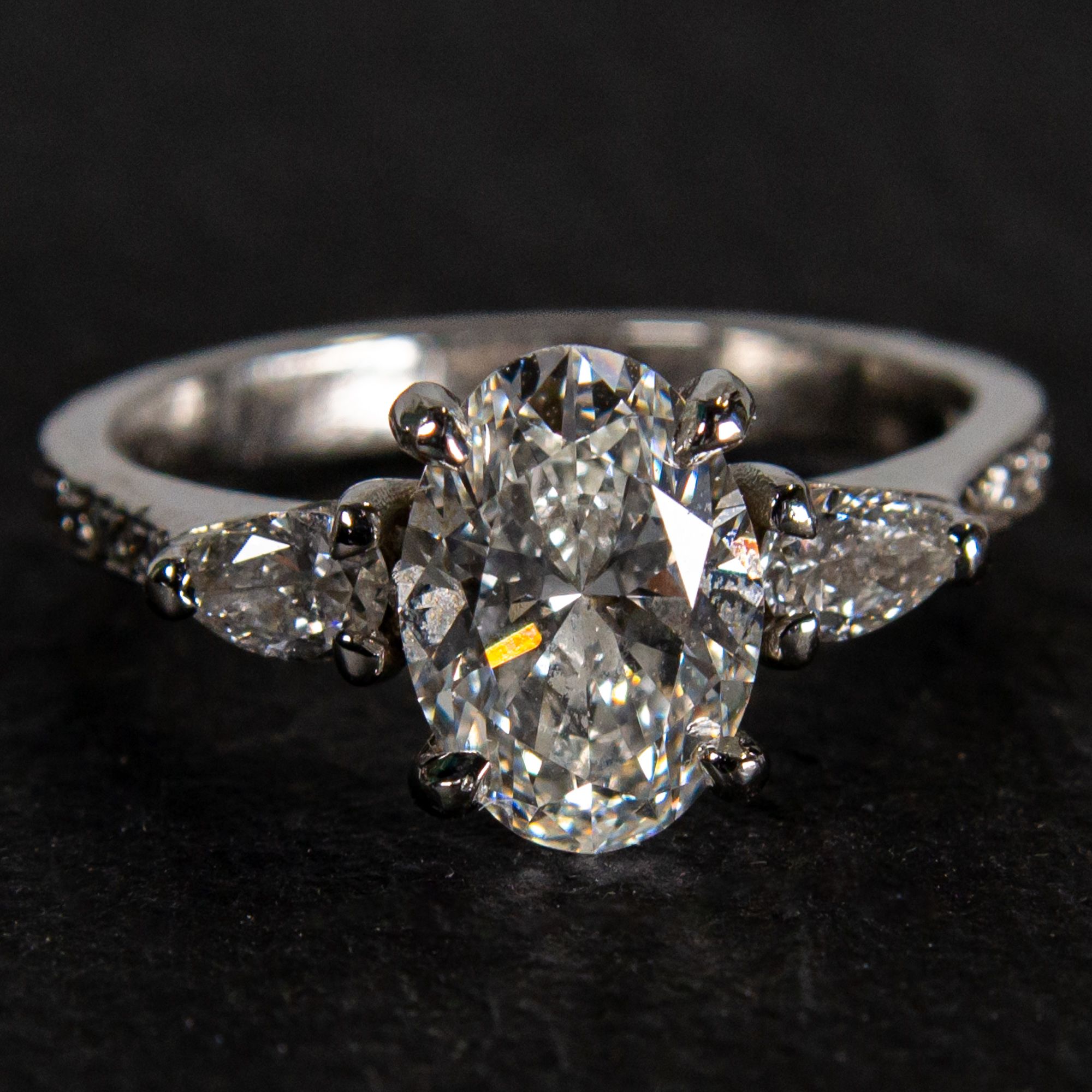 Handmade platinum engagement ring featuring an oval centre diamond with pear shaped diamond side stones and diamond set shoulders
