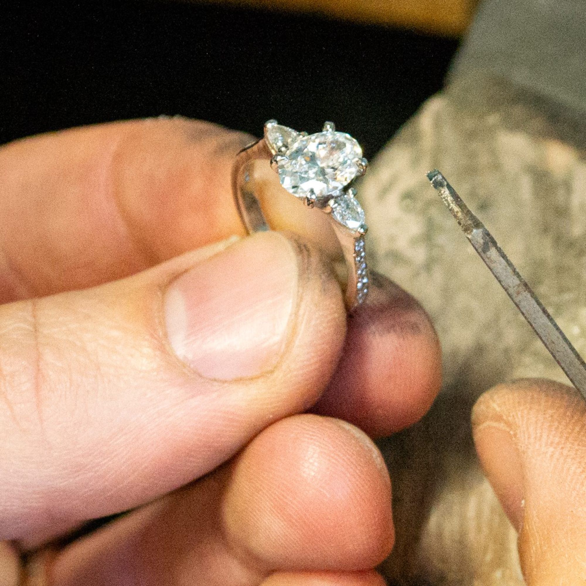 Close up of a goldsmith hand finishing a diamond engagement ring at the bench in a Wiltshire workshop, filing the setting in recycled precious metal