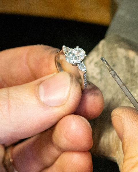 Close up of a goldsmith hand finishing a diamond engagement ring at the bench in a Wiltshire workshop, filing the setting in recycled precious metal