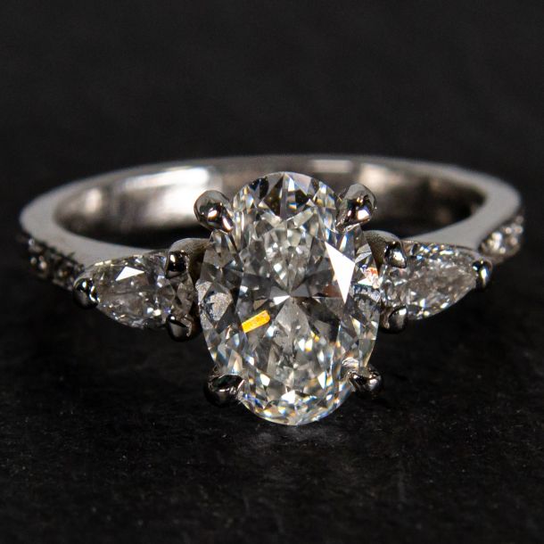 Handmade platinum engagement ring featuring an oval centre diamond with pear shaped diamond side stones and diamond set shoulders