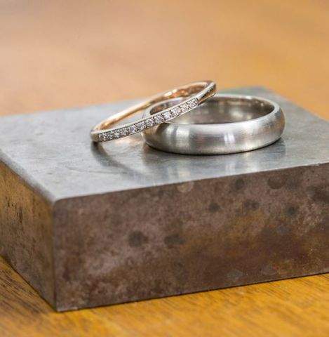 Diamond wedding band and brushed metal wedding ring displayed on a jeweller's steel block