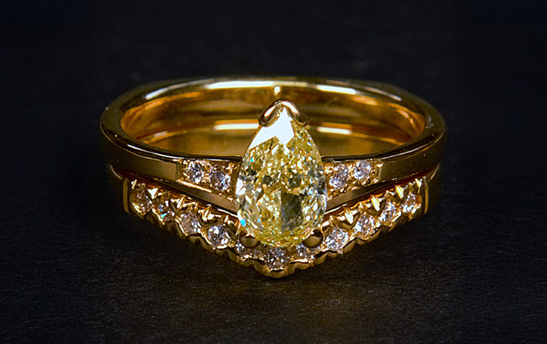 Yellow gold engagement ring set featuring a pear shaped yellow diamond with matching diamond wedding band on a dark background