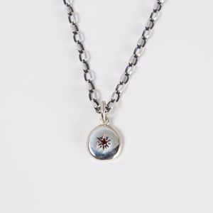 Seidr Frum Birthstone Charm in recycled sterling silver set with garnet shown on chain, a small pebble talisman handcrafted in Wiltshire