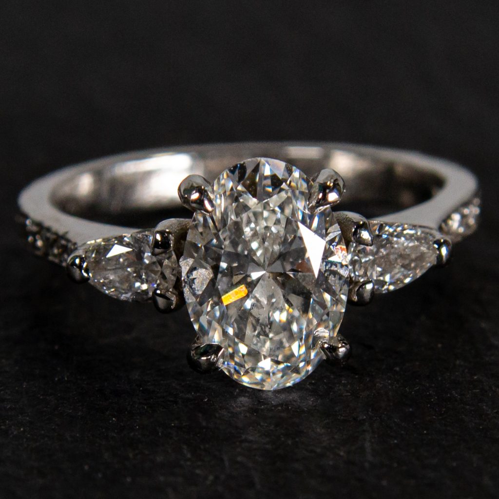 Handmade platinum engagement ring featuring a 2ct oval centre diamond with pear shaped diamond side stones and diamond set shoulders