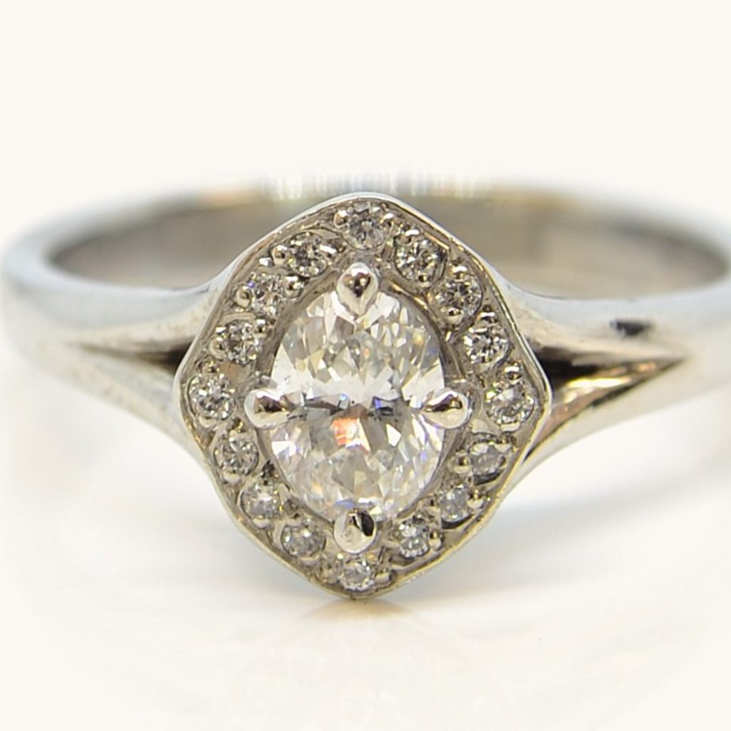 Oval diamond halo engagement ring in white gold with a claw-set centre diamond surrounded by a pavé diamond halo