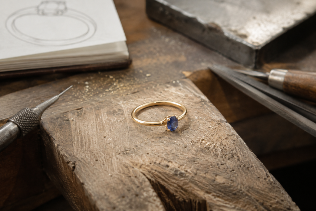 Simple 9ct yellow gold engagement ring with small blue gemstone on a jeweller’s bench