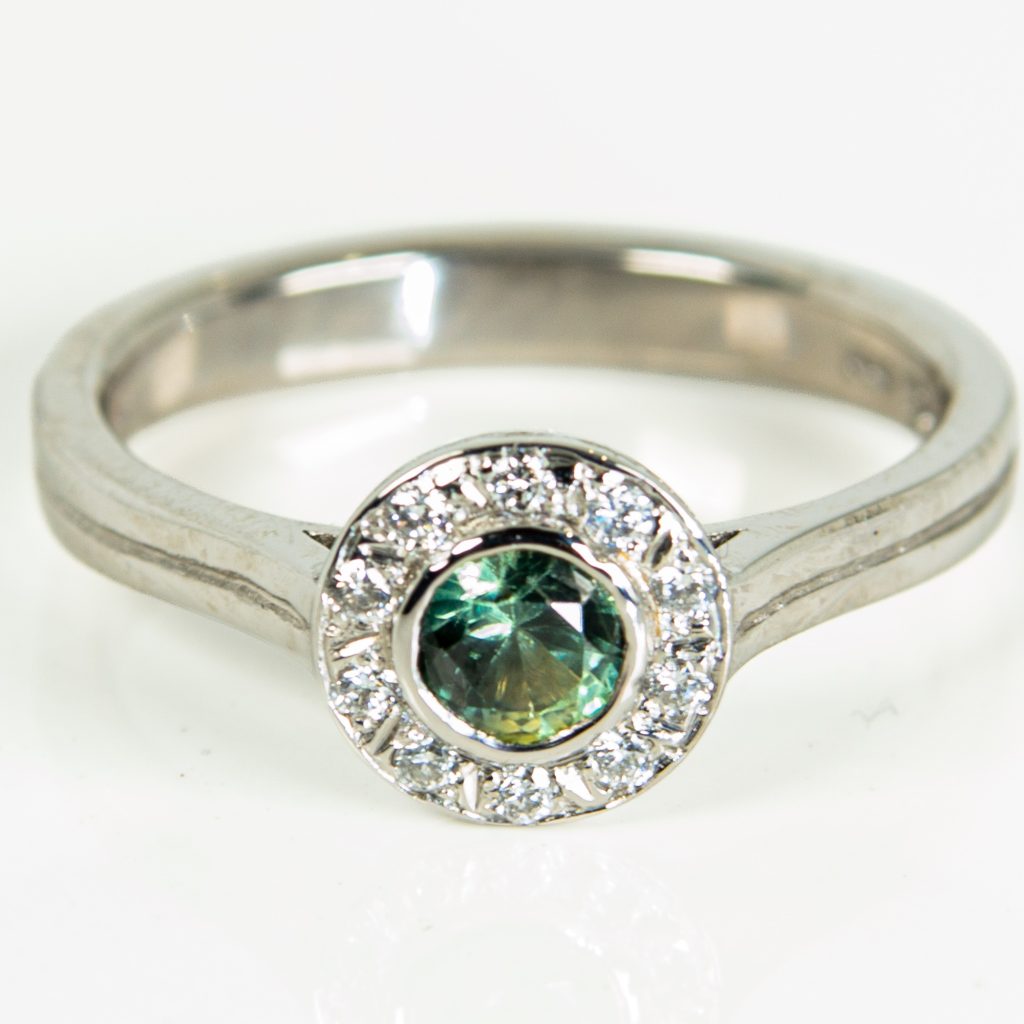 Platinum engagement ring with a green sapphire in a rub-over setting, surrounded by a diamond halo